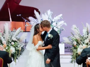 Bride and Groom share their first kiss during the ceremony surrounded by large stunning floral arrangements | Insert Wedding Flowers | Photo Credit: Becky Lee Brun